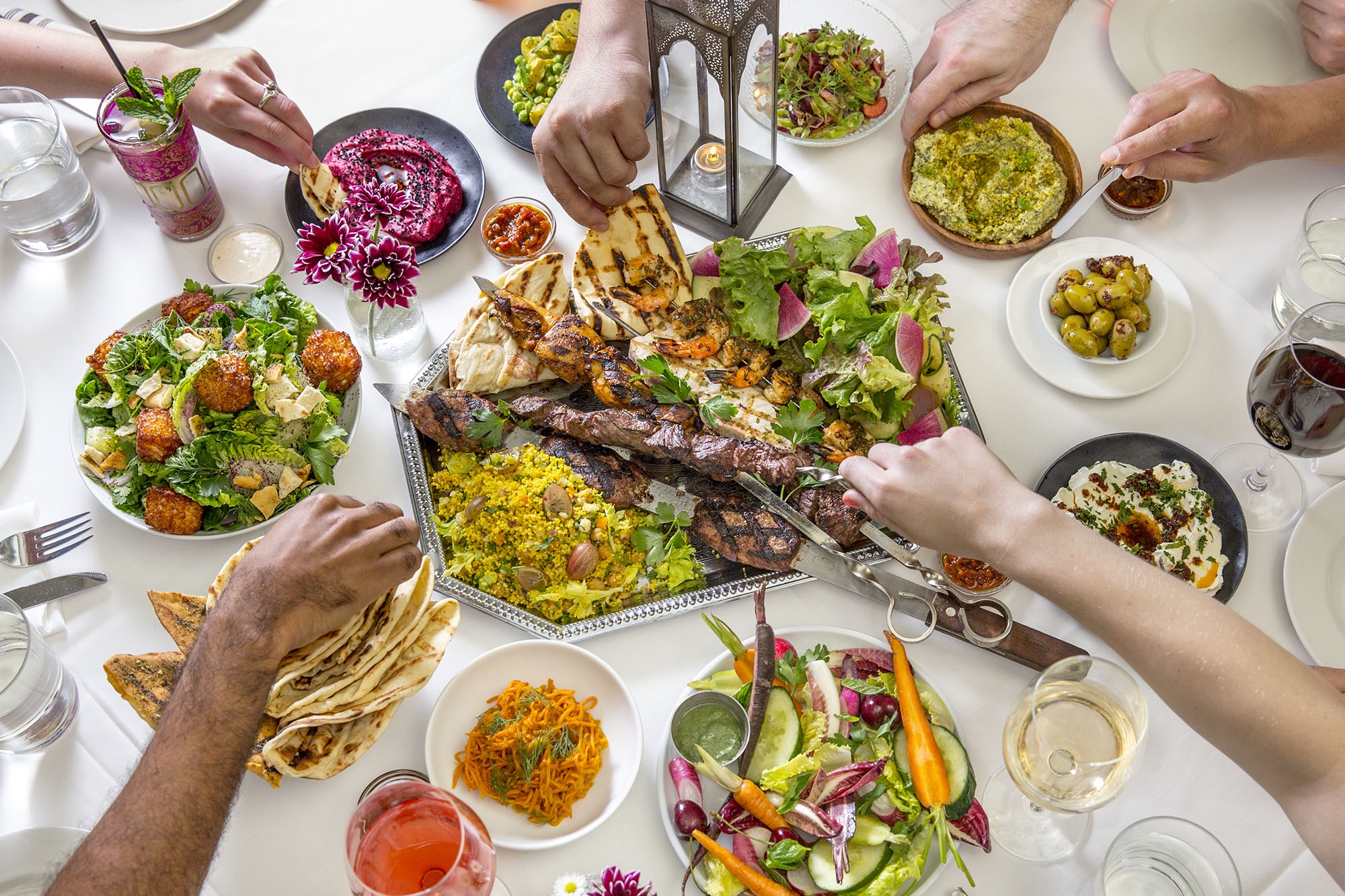 A group of people reaching for greek food at the restaurant Shuka.