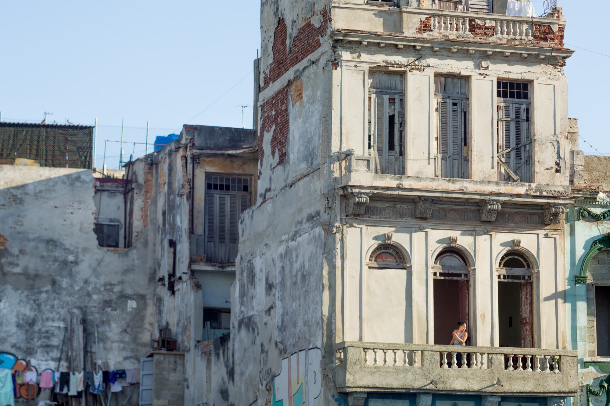 A woman standing in a window of a run down mansion in Havana.