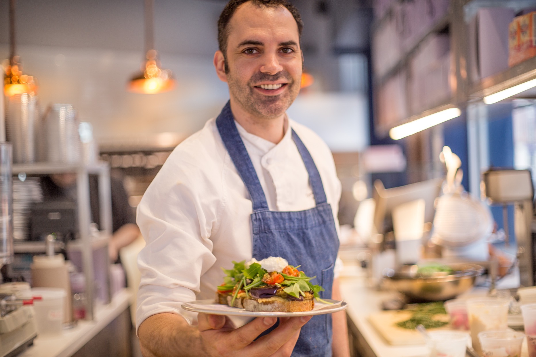 A photograph of chef Dominique Ansel holding out a plate of food.