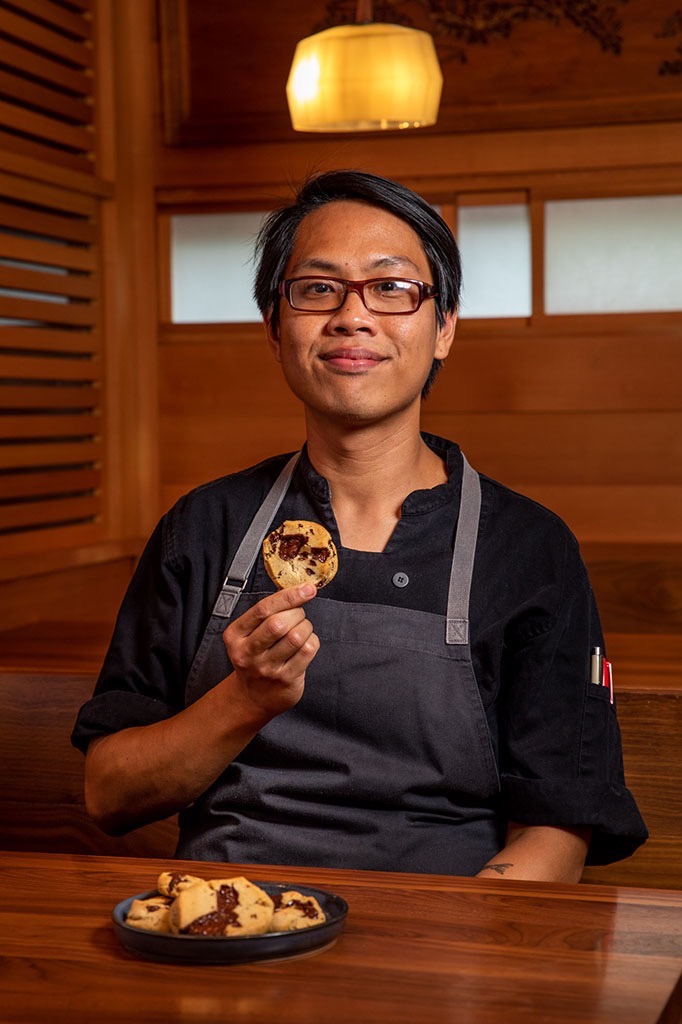 A pastry chef posing for a portrait with a cookie that he made