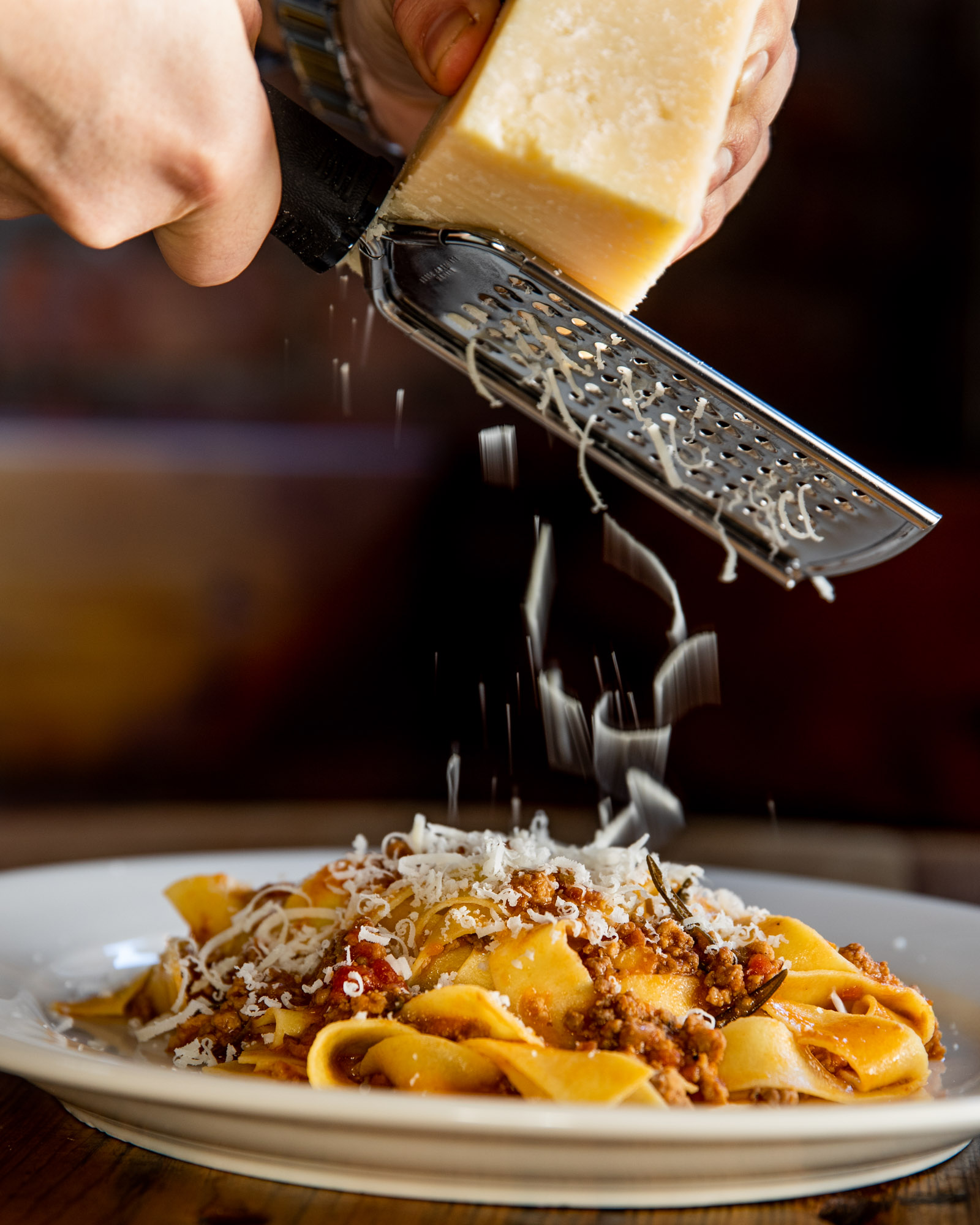 Cheese being grated over a bowl of pasta at Convivium Osteria.